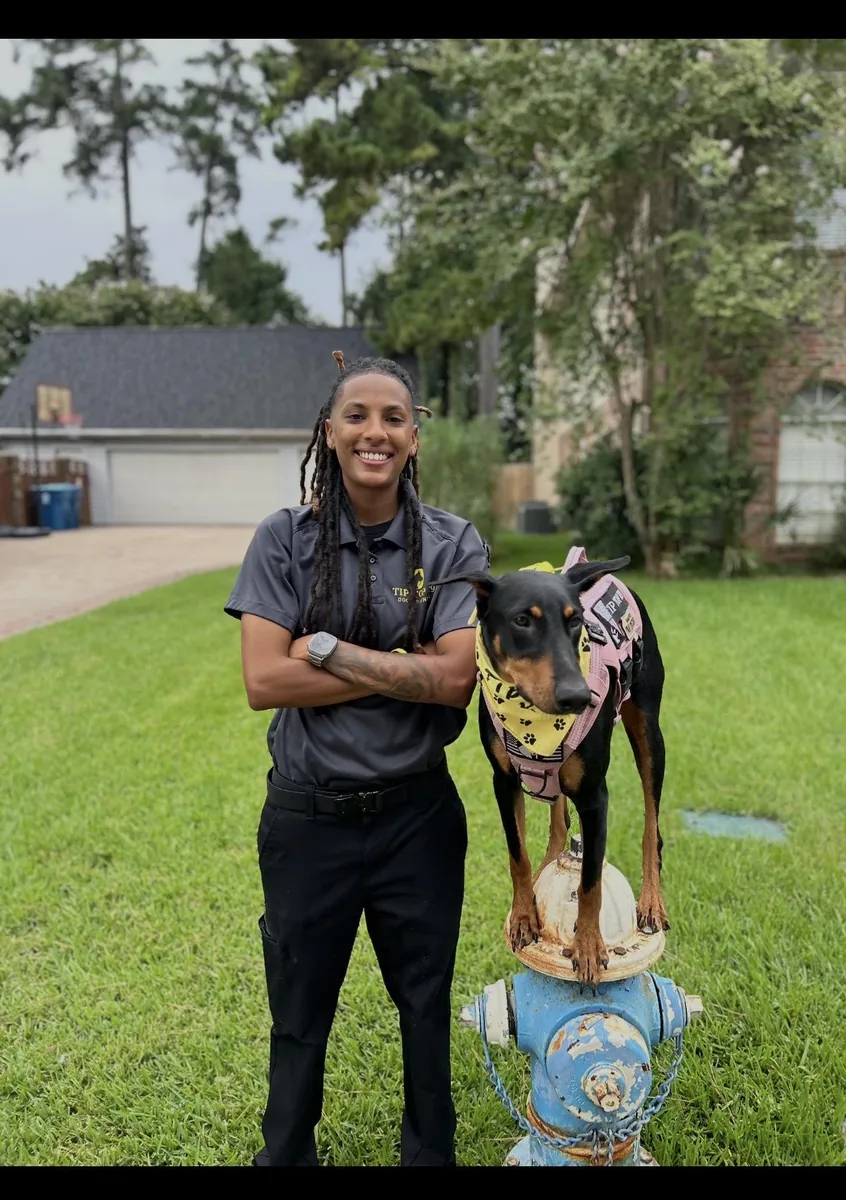 Yaya Villar, dog trainer at Tip Top K9 Humble, with a Doberman balanced on a fire hydrant